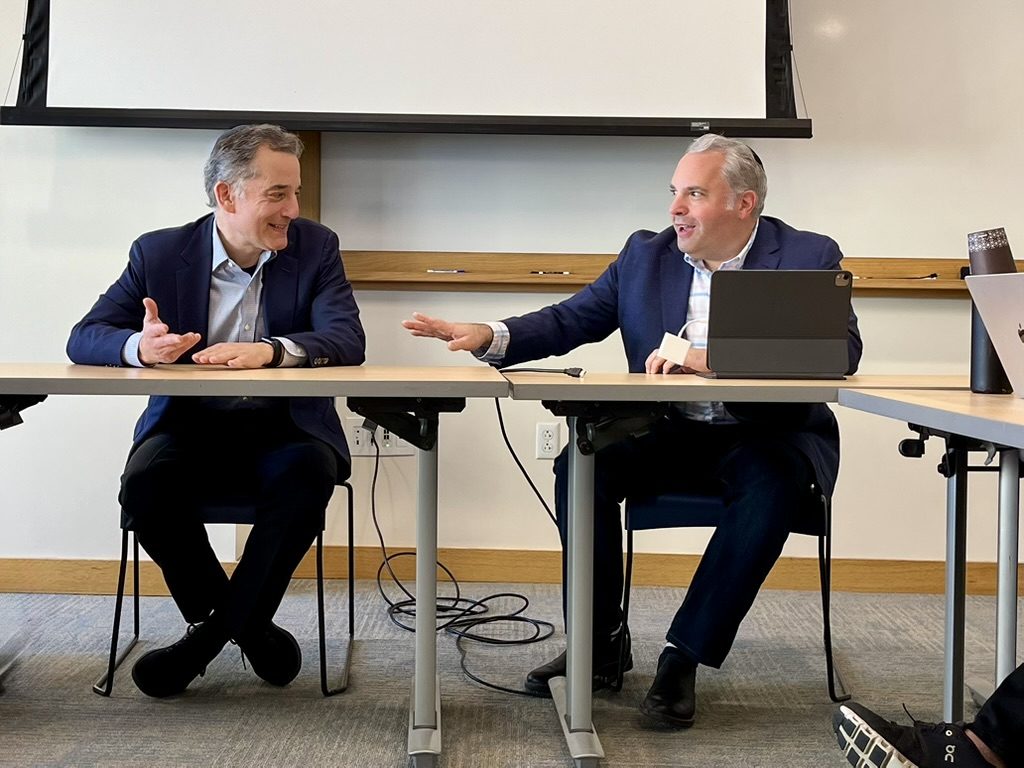 Gideon Zelermyer and Rabbi David Wolpe seated at a seminar table, both mid-sentence, gesturing at one another.