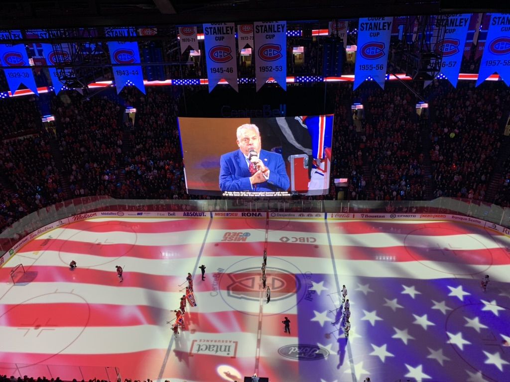 The Bell Centre from high in the stands, the Stars and Stripes projected across the whole ice surface, the cantor on the jumbotron.