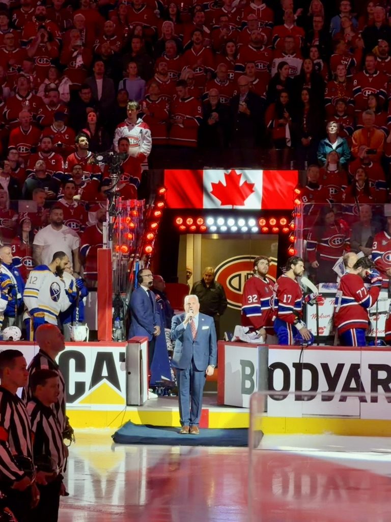 Alone at centre ice in a blue suit and kippah, singing, the teams lined up behind.