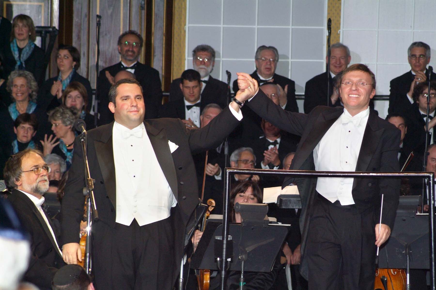 Zelermyer in white tie taking a bow hand in hand with Stephen Glass, the chorus applauding behind them.