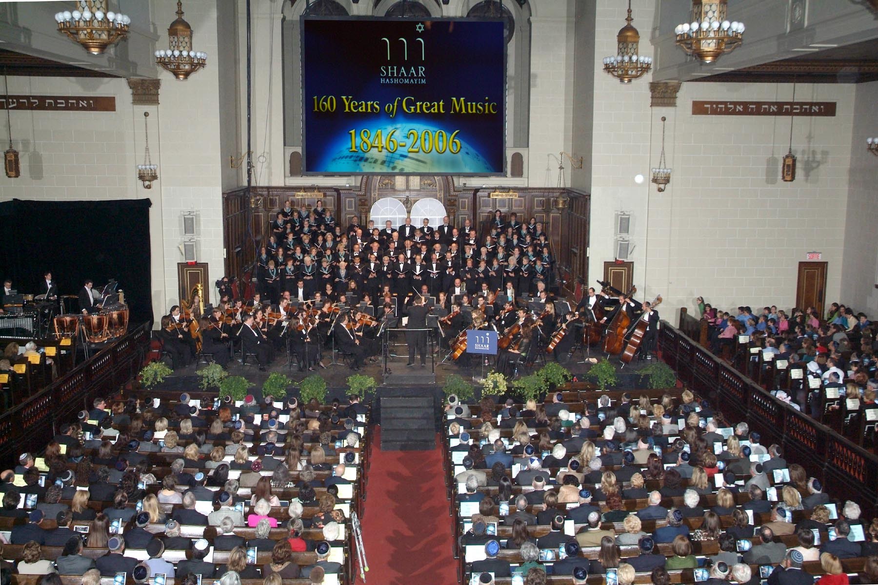 The sanctuary from the balcony: a full chorus banked before the ark, symphony orchestra in front of them, every pew occupied, and a screen above reading 160 Years of Great Music, 1846&ndash;2006.
