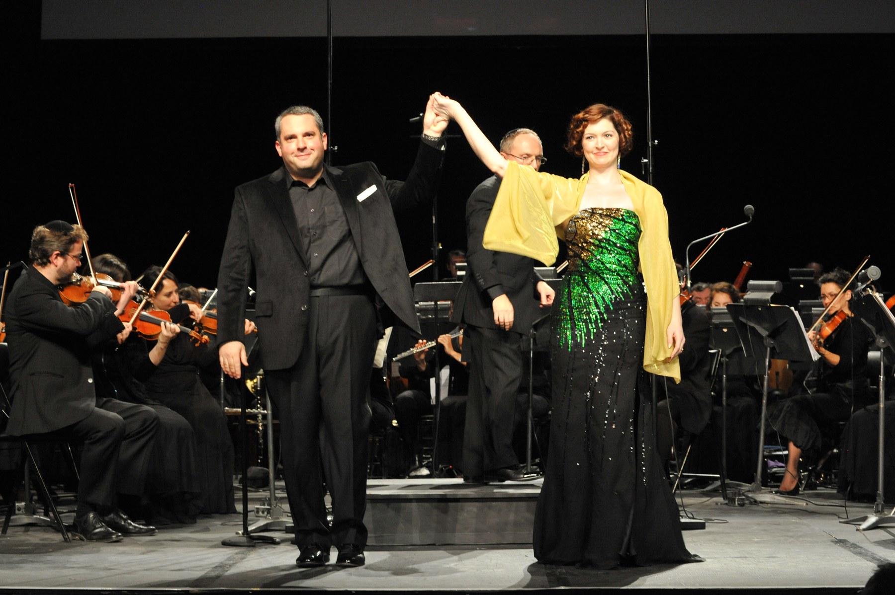 Zelermyer and Leah Edwards taking a bow hand in hand, the orchestra behind them, Stephen Glass between them.