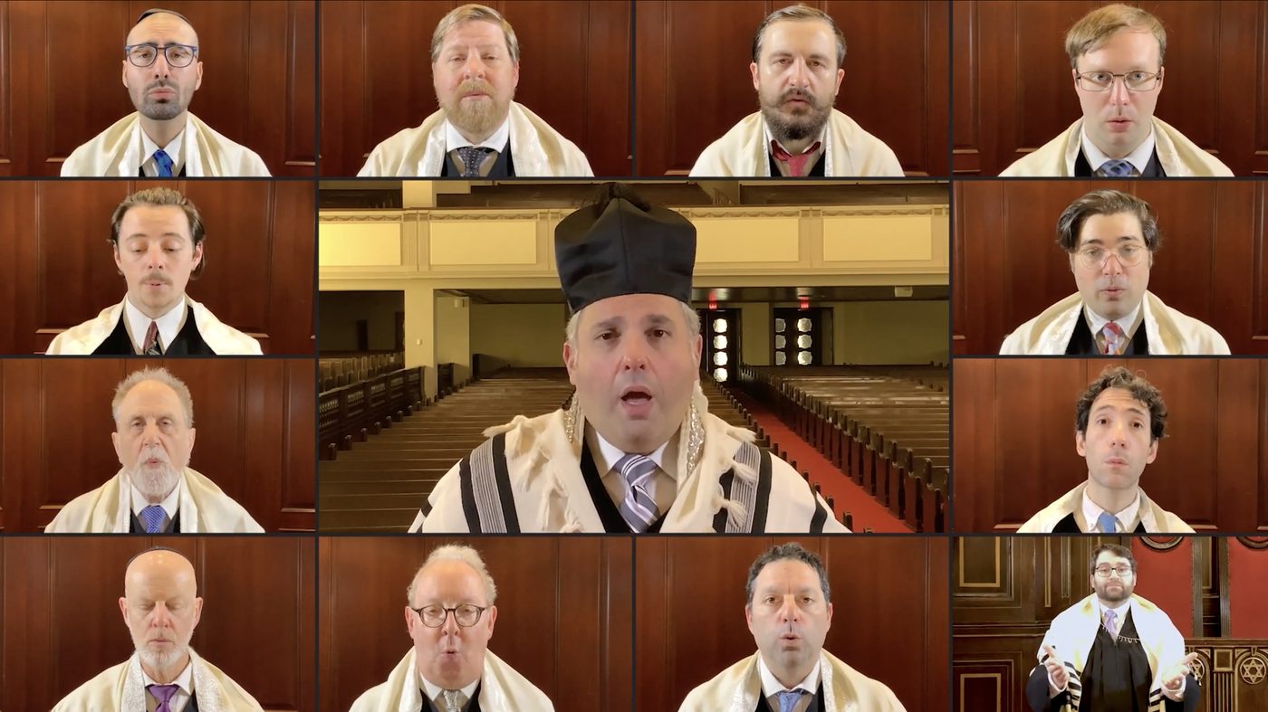 Twelve boxes on one screen: eleven choristers in prayer shawls, each filmed against the sanctuary panelling, and at the centre the cantor in his hat before the empty pews.