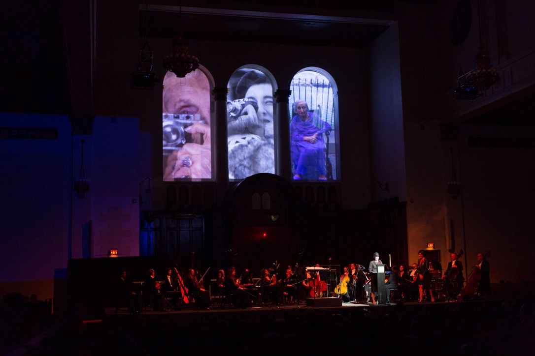 Three arched windows filled with projected images of one of the women, holding a camera, in fur, and in old age.