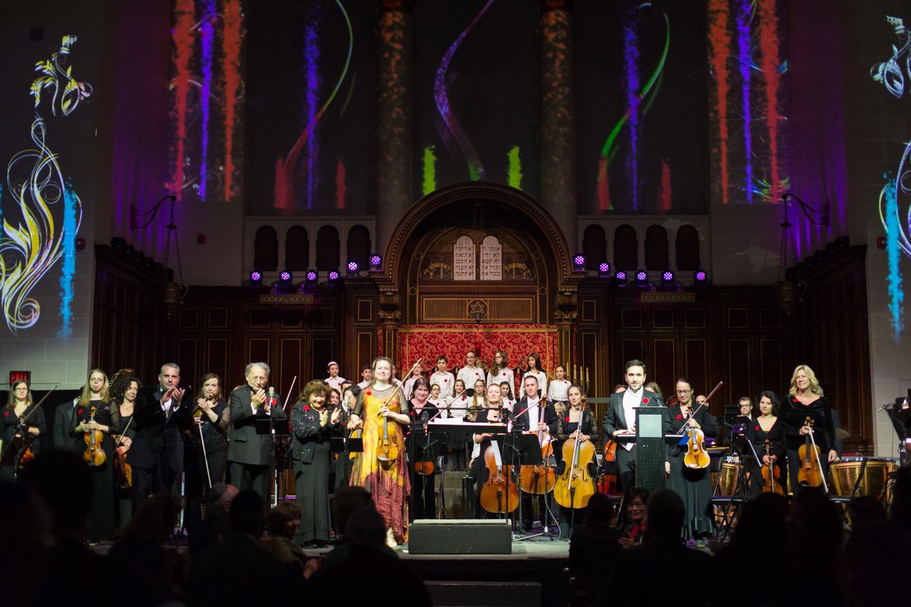 The company taking a bow — orchestra, soloists and children's choir — beneath vivid projections running up the sanctuary columns.