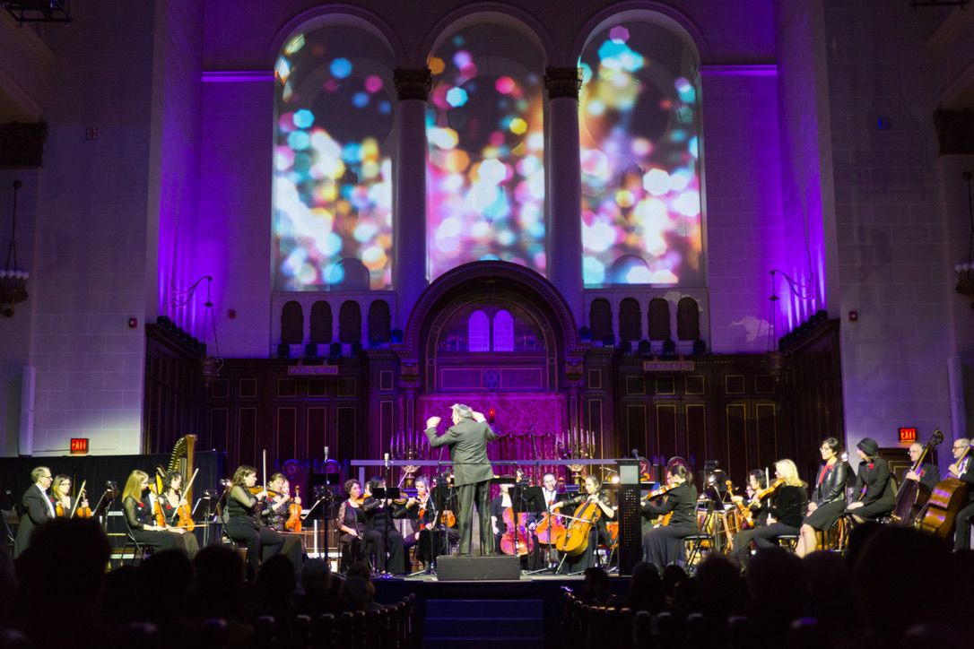The McGill Chamber Orchestra playing beneath three arched windows filled with projected points of coloured light.