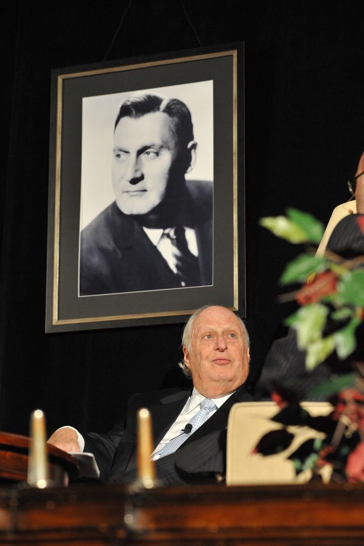 Barry Tucker seated on stage beneath a large framed portrait of his father, Richard Tucker.