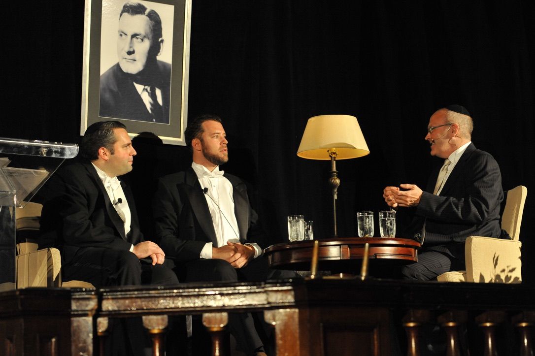 Gideon Zelermyer and Joseph Kaiser in white tie seated in armchairs opposite the host Kelly Rice, a portrait of Richard Tucker hanging behind them.
