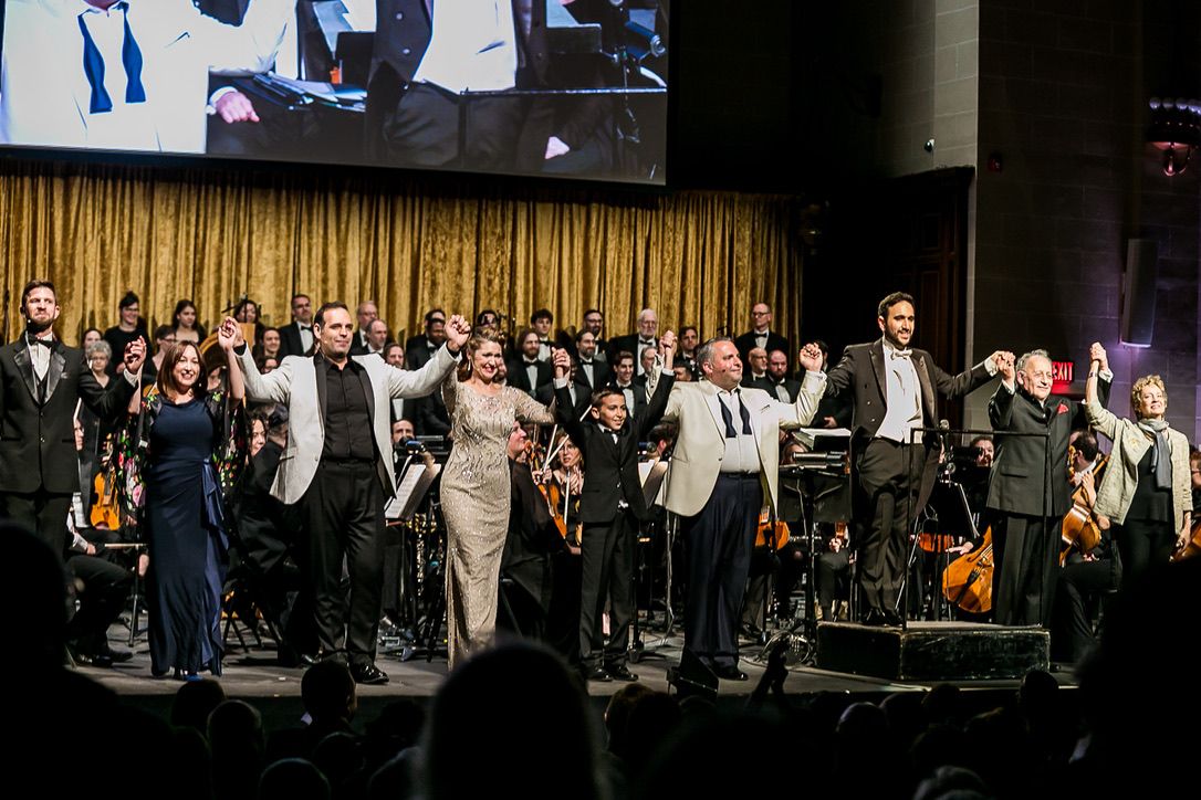 The full company at the curtain call, hands joined and raised — soloists, choirs, orchestra and conductors.