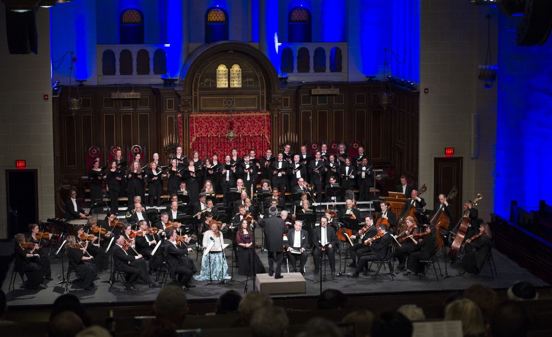 Orchestra and chorus arrayed before the ark, its red curtain and the tablets of the Law visible above.