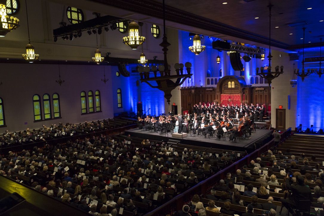 The Orchestre symphonique de Montréal playing on a stage built over the bimah of the Shaar Hashomayim sanctuary, the pews full, the walls lit blue.