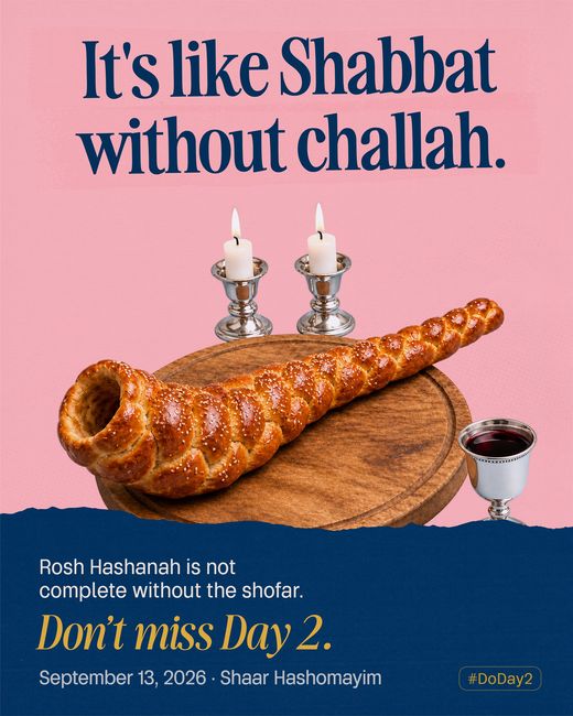 A braided challah curved into the shape of a shofar on a wooden board, with two lit Shabbat candles behind it and a silver kiddush cup beside.