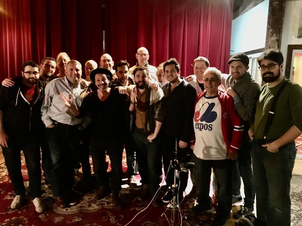 Some eighteen people — the Shaar Hashomayim choir, Adam Cohen and the studio crew — posed together in front of a red curtain in a Montreal recording studio.
