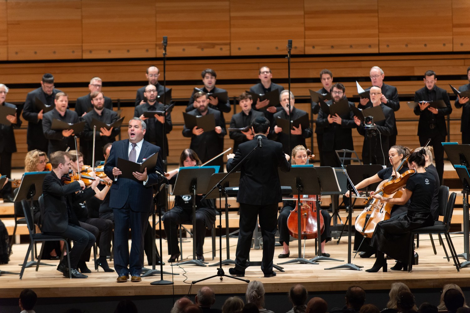 Zelermyer singing from a score at the front of the Maison symphonique stage, Ro&iuml; Azoulay conducting with his back to the camera, the Shaar Hashomayim choir banked on risers behind and the orchestra either side.