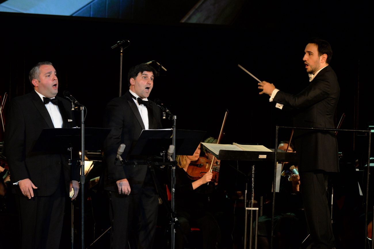 Gideon Zelermyer and Netanel Baram singing side by side at their music stands, Roï Azoulay conducting at right with his baton raised.