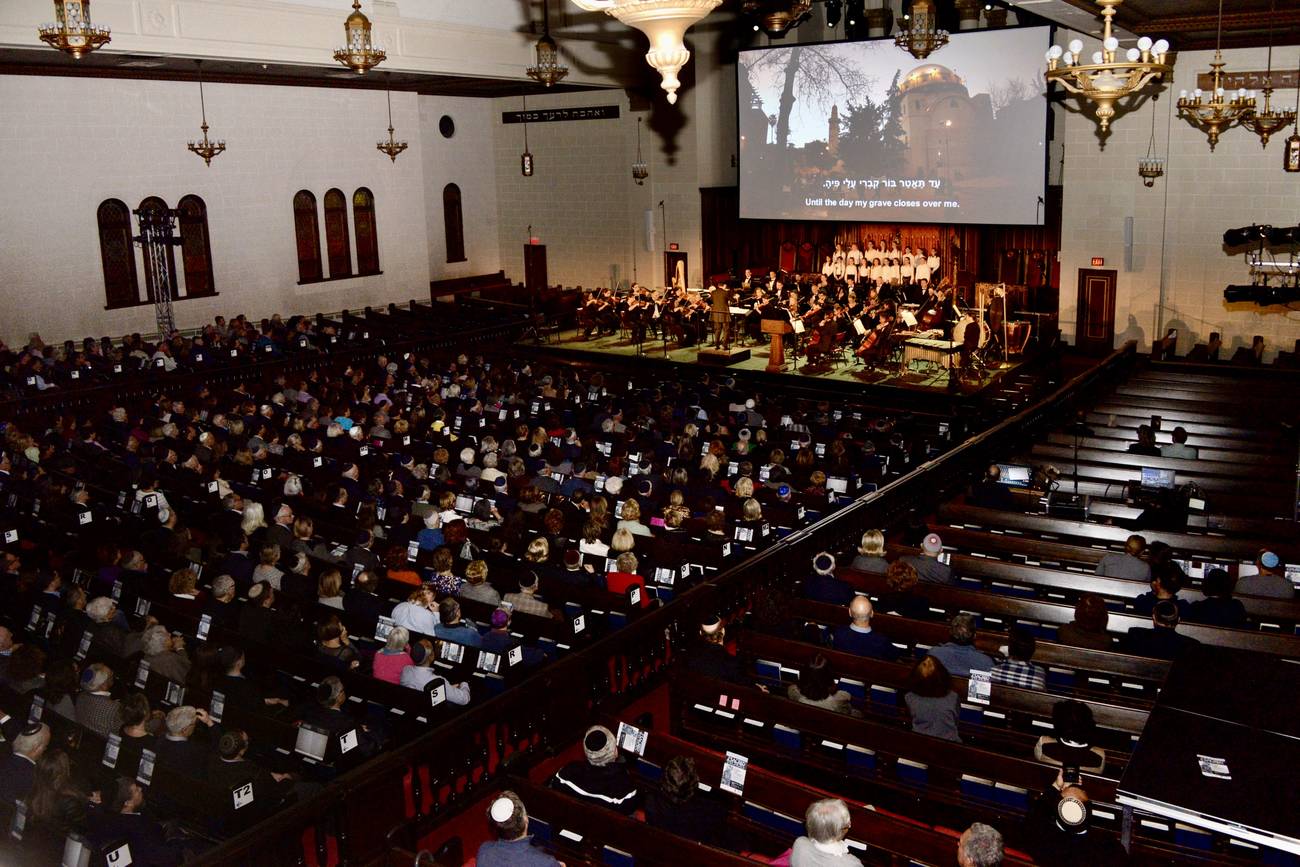 The sanctuary seen from the balcony, pews full to the back, the orchestra and children's choir on a stage built over the bimah beneath a wide projection screen.