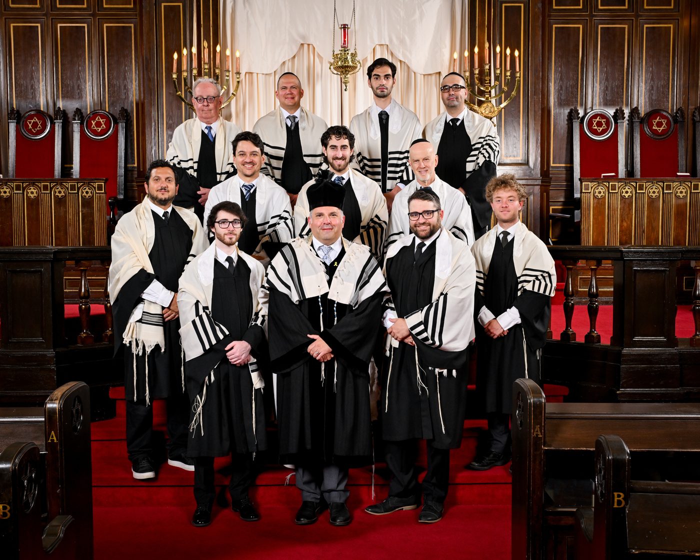 Gideon Zelermyer in cantor&rsquo;s robes and hat with the Shaar Hashomayim Synagogue Choir in robes and tallitot, standing on the bimah before the ark.