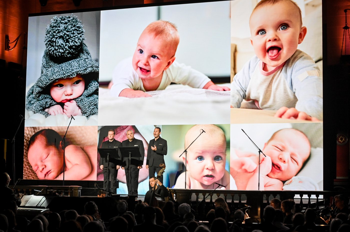 The three cantors dwarfed by a grid of six enormous photographs of babies filling the video wall behind them.